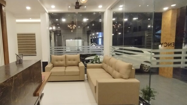 Uma área de recepção de hotel com balcão, sofás bege e uma grande janela com vista para um carro e um edifício com a inscrição "RESTONE INN".