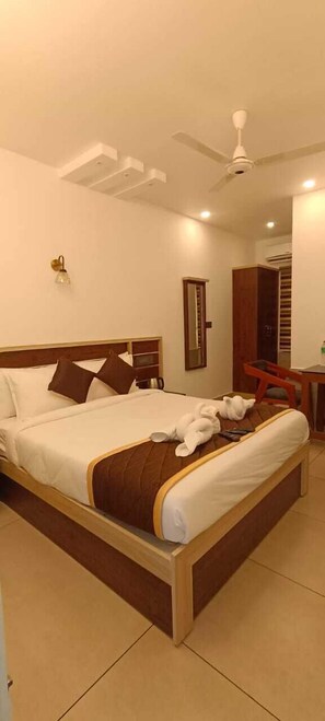 A hotel room with a bed, a desk, a chair, a ceiling fan, and a wall-mounted light. - Paul residency (Aluva)