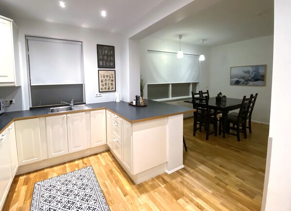 A modern kitchen with white cabinets, a wooden countertop, and a dining area with a table and chairs. - Day Dream Apartments Laugavegur 139 (Reykjavik)
