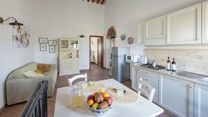 A spacious kitchen with white cabinets, a dining table set with fruits and a pitcher, and a cozy living area with a sofa and a teddy bear. - Bellavista at Podere il Moro (Toscana)