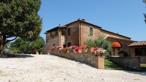 A stone building with a tiled roof, a gravel driveway, and flowering plants along the front. - Bellavista at Podere il Moro (Toscana)
