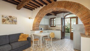 Eine Küche mit einer Ziegelbogenarchitektur, weißen Schränken, einem Esstisch mit Stühlen und einem grauen Sofa mit gelbem Kissen.