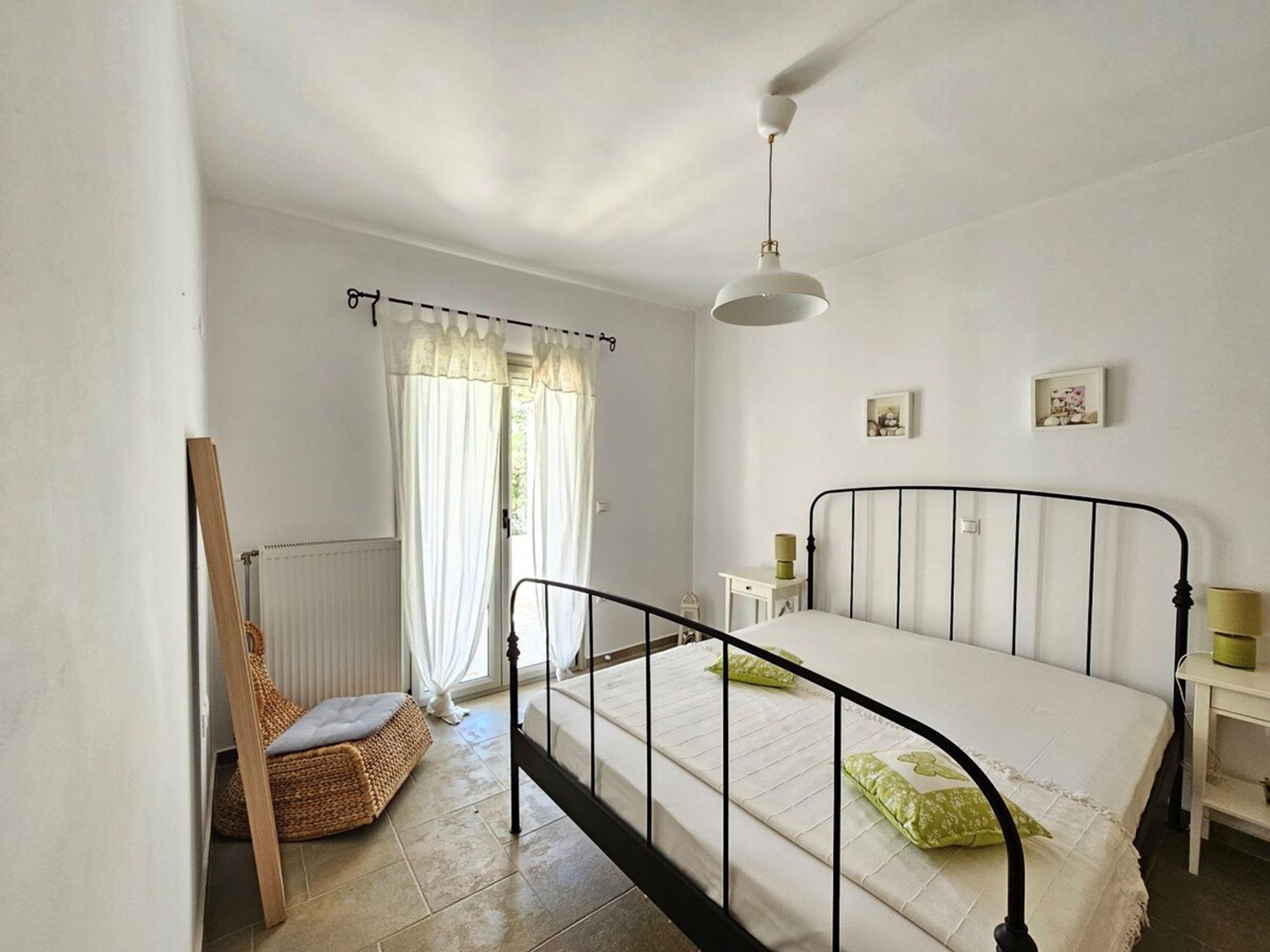 A bedroom with a bed, a chair, a radiator, a window with curtains, and a ceiling fan.