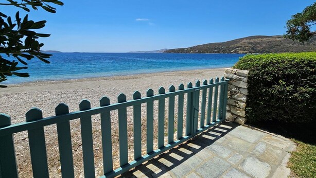 A pebble beach with a stone pathway and a green fence leading to the sea.