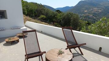 A balcony with two wooden chairs and a small round table, overlooking a mountainous landscape.