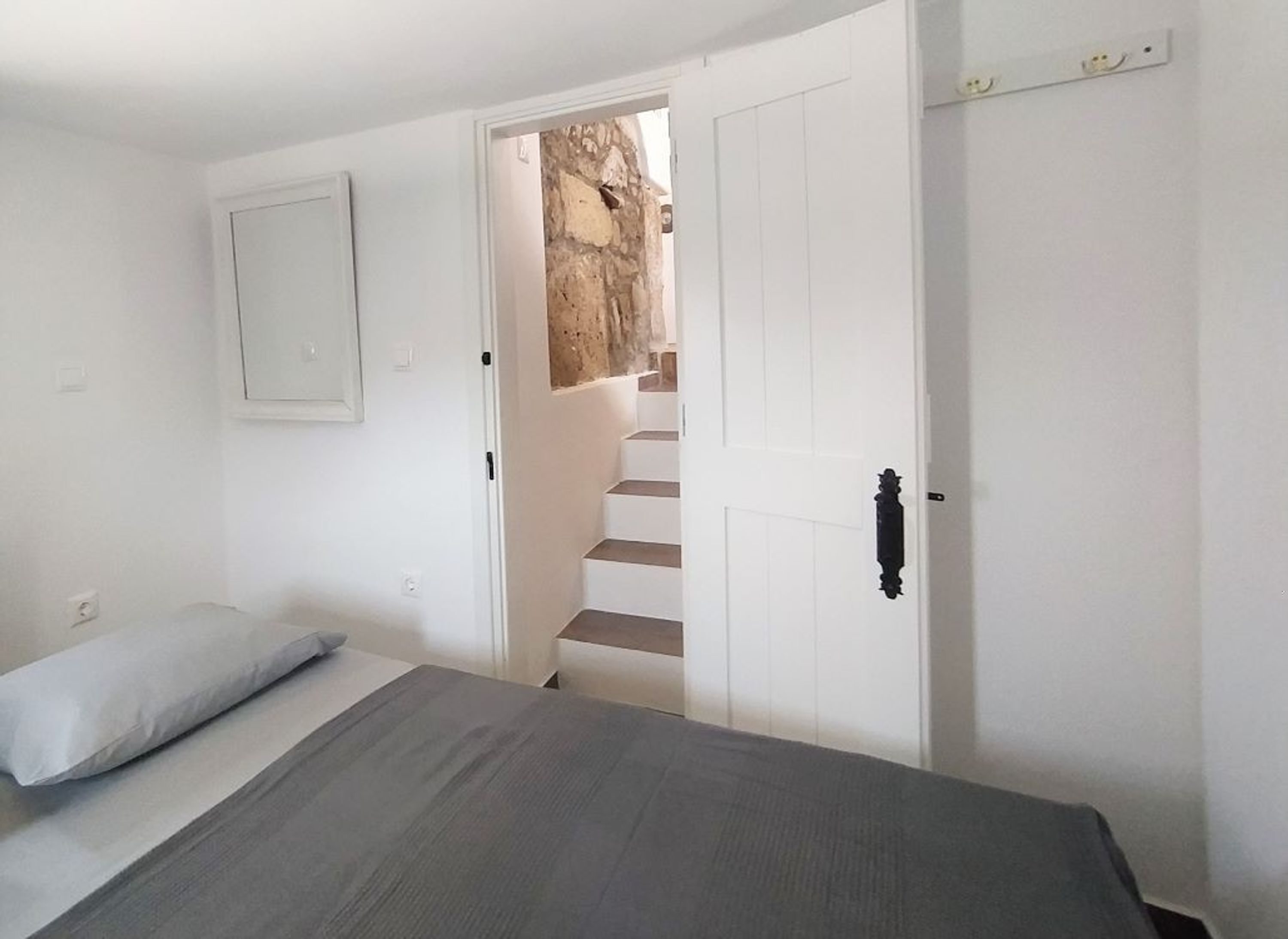 A bedroom with a bed, a white door, and a staircase leading to a stone wall.