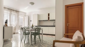 A modern kitchen with white cabinets, a wooden door, and a dining area with a table and chairs. - 4065 Kalès Holiday by Barbarhouse (Otranto)