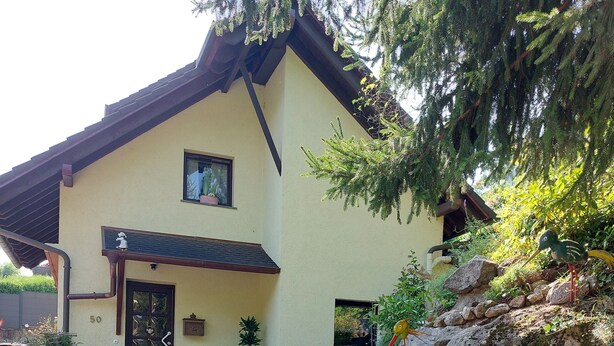 A house with a sloped roof, a front porch with a bench, and a stone staircase leading to the entrance. - Ferienhaus "gängelbach" Auszeit im Grünen bei Bachrauschen! (Weinheim)