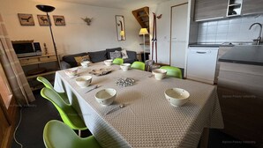 A compact living space with a dining table set for four, green chairs, a kitchenette, and a TV in the corner. - Duplex apartment 45m², 3 rooms, 8 ppl, balcony, near slopes, pets allowed (Peisey-Vallandry)
