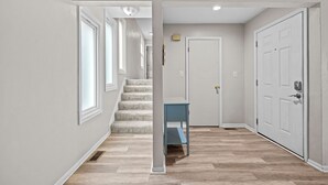 Un pasillo con una escalera, una puerta y una mesa azul.