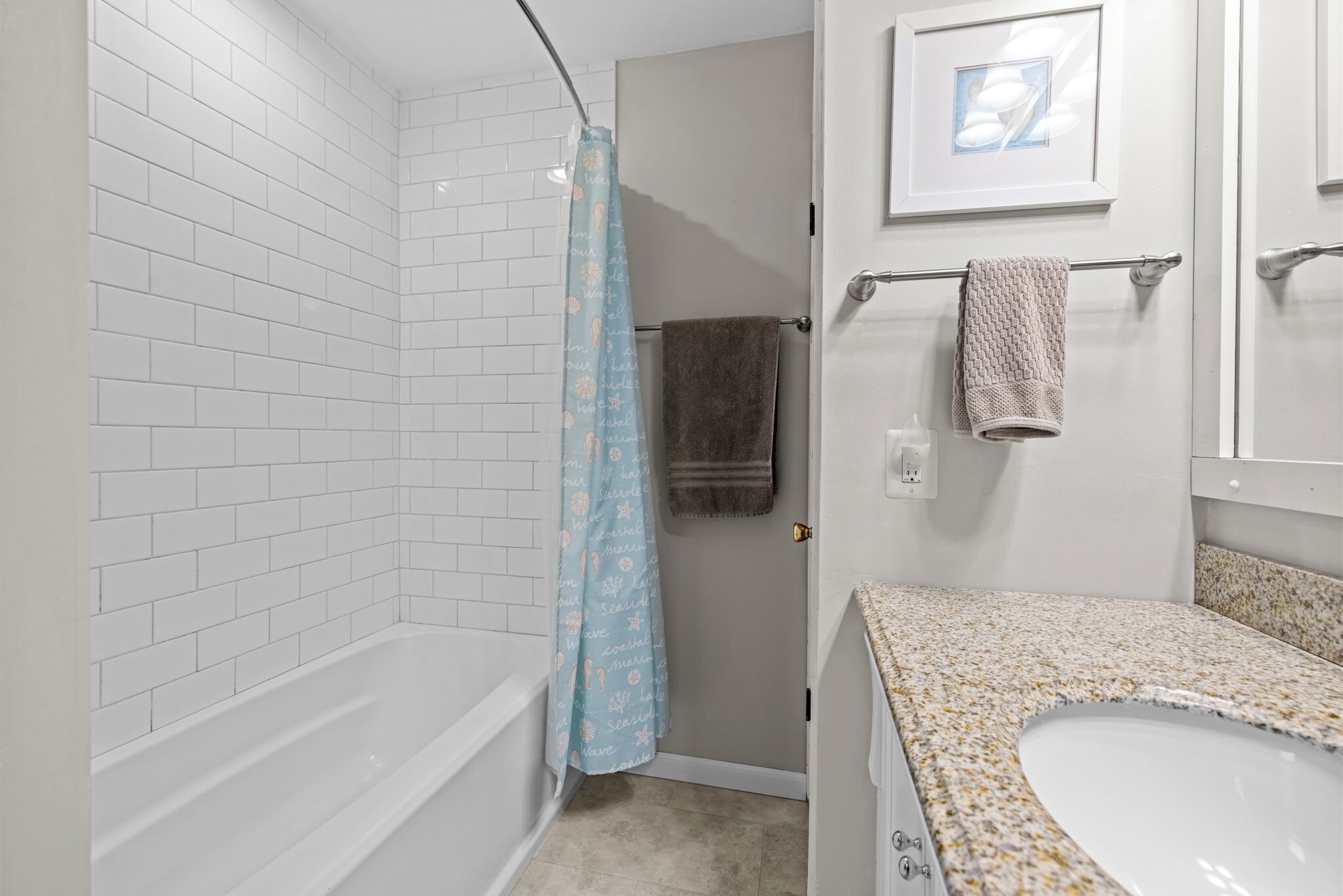 A bathroom with a white tiled shower, a bathtub, a sink with a granite countertop, and a towel rack with towels.