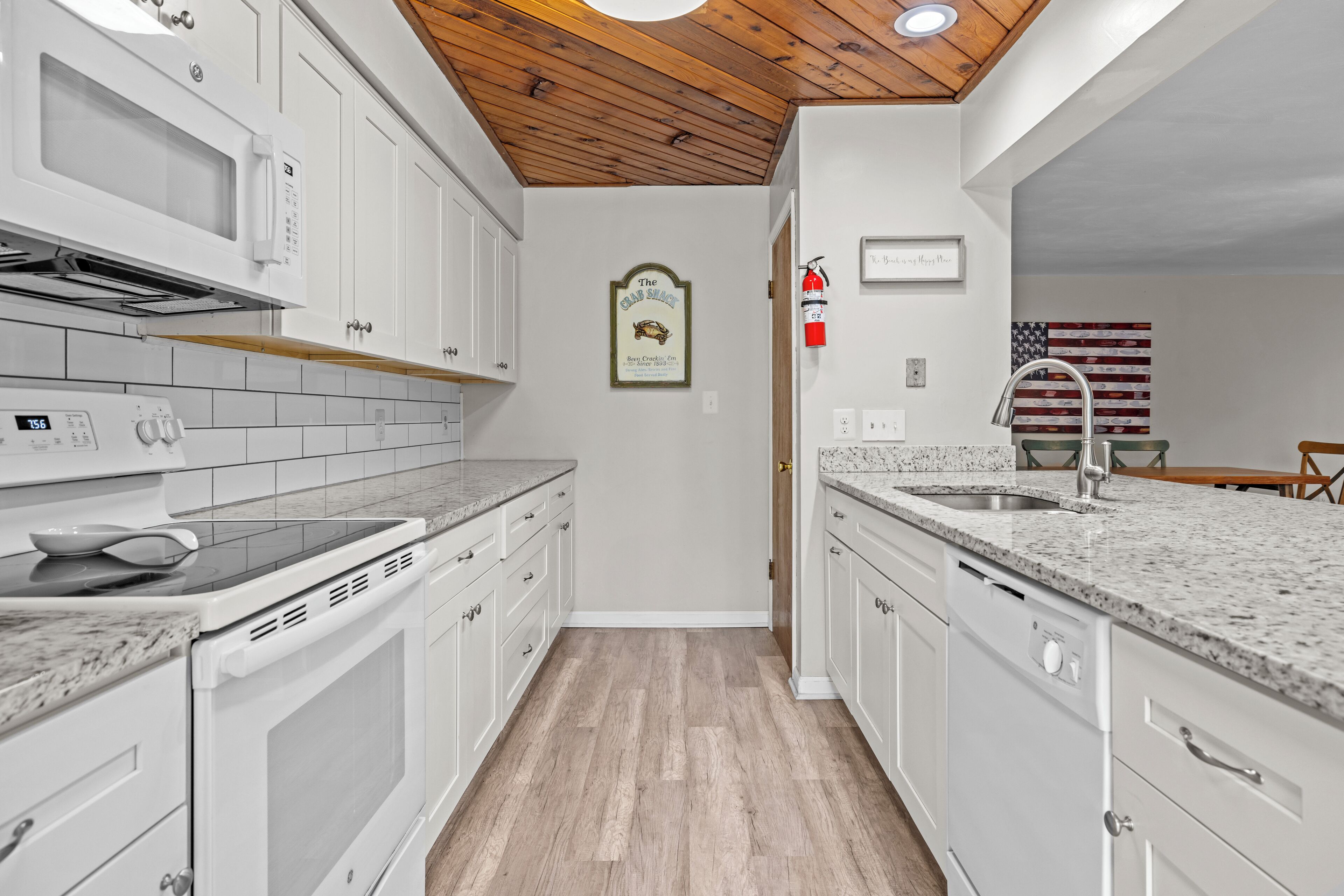 Una cocina con armarios blancos, encimera de granito, microondas, horno y lavabo.