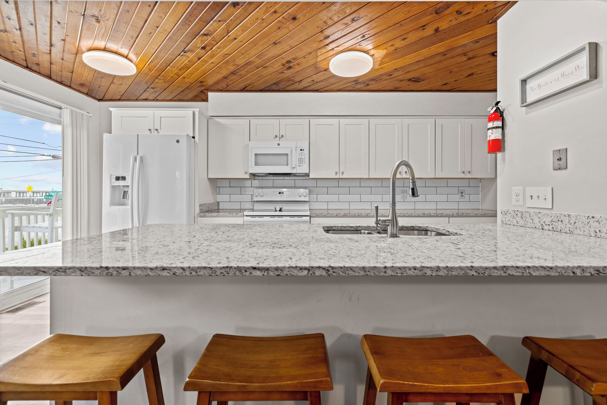 A kitchen with white cabinets, a granite countertop, a stainless steel sink, and wooden stools.