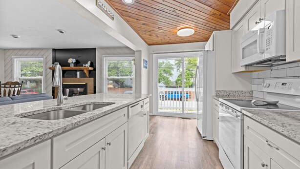 Una cocina moderna con armarios blancos, encimeras de granito y techo de madera.