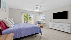 Un dormitorio con cama, ventilador de techo, televisor, silla y ventana con cortinas.