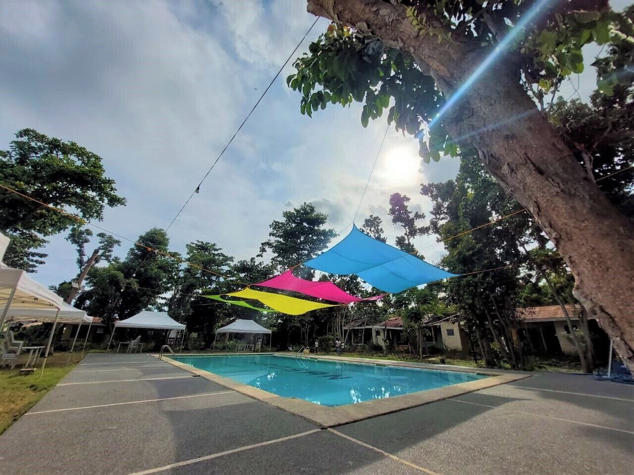 A swimming pool with colorful canopies, surrounded by trees and white tents.
