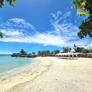 A beach with clear turquoise water, a sandy shore, and a white tent structure. - The Beach Park hadsan by Hiverooms (Lapu-Lapu)