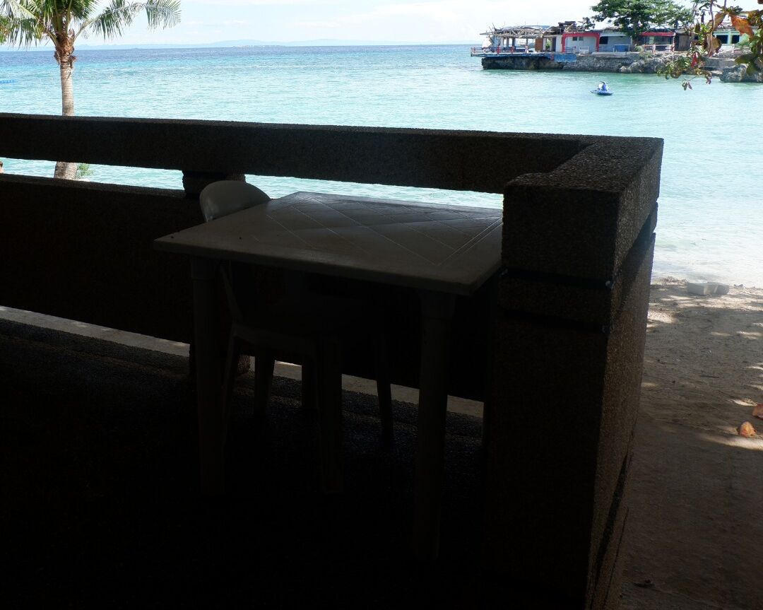 Un banco con vistas a una playa y al océano, con un barco a lo lejos.