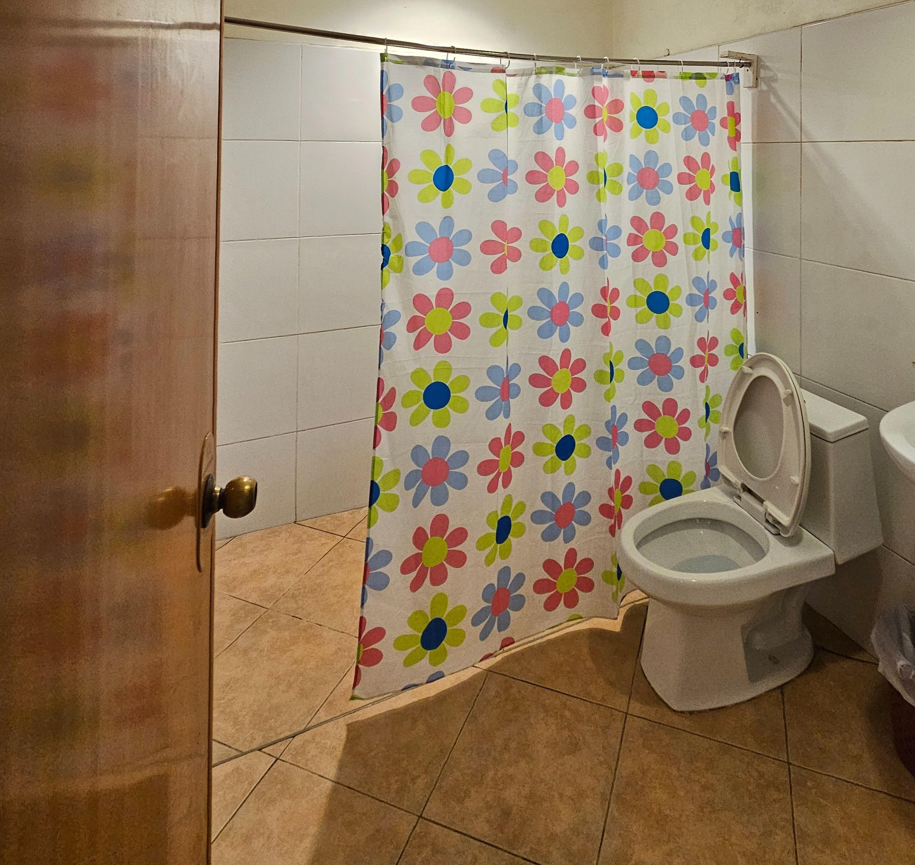 A bathroom with a shower curtain featuring a colorful flower pattern, a toilet, and a tiled floor.