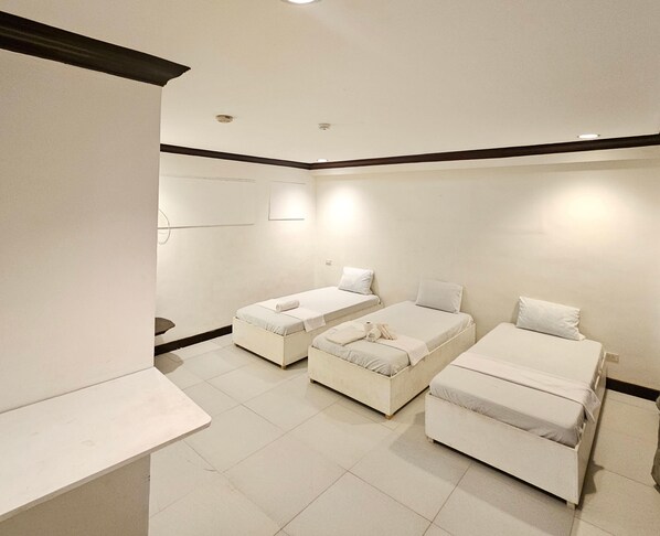 A hotel room with three single beds, a small table, and a large mirror.