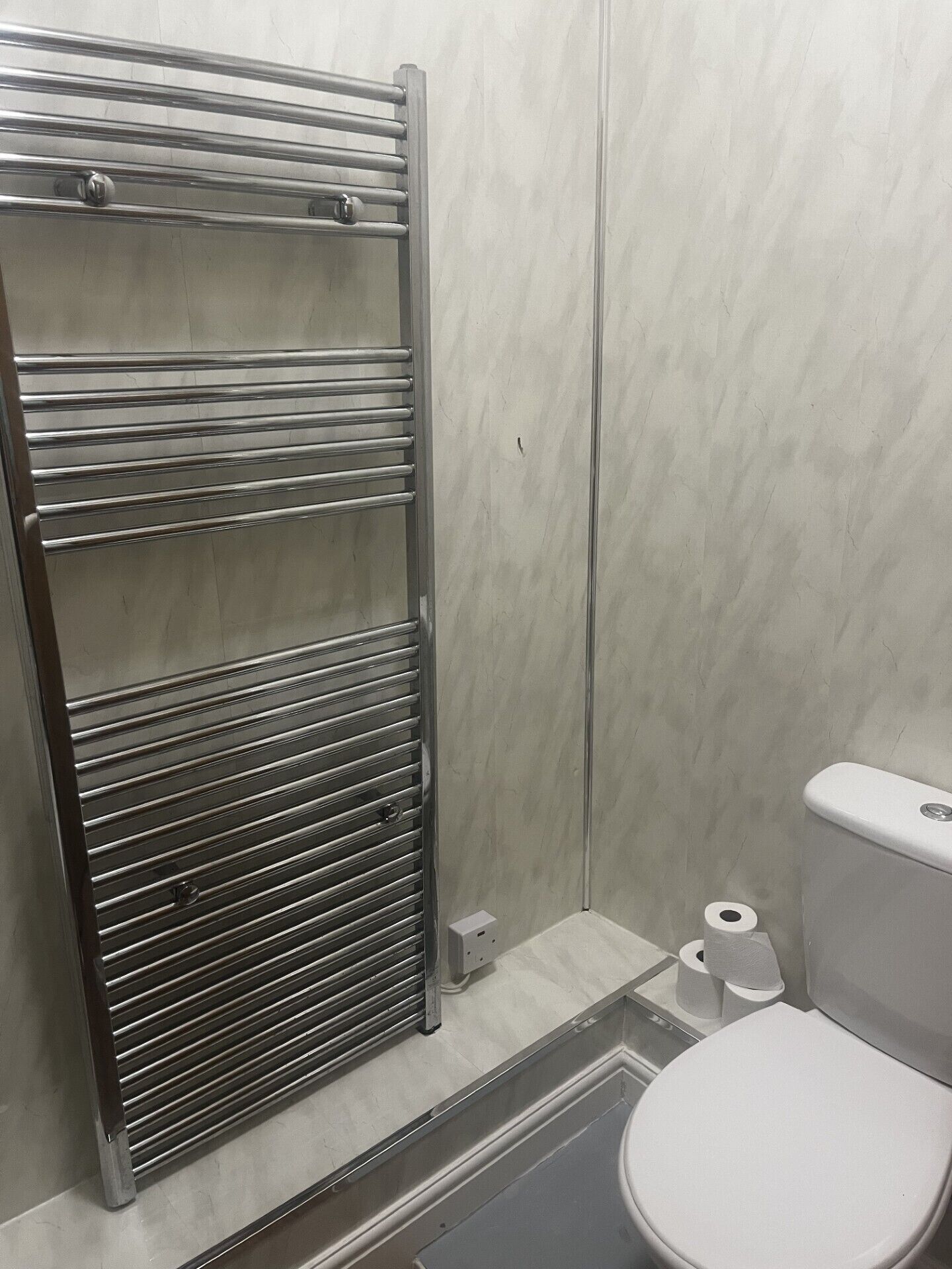 Een badkamer met een handdoekhouder van roestvrij staal, een toilet en een kleine prullenbak.