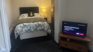 Una habitación de hotel con una cama, un televisor sobre un soporte y una puerta que da a otra habitación.