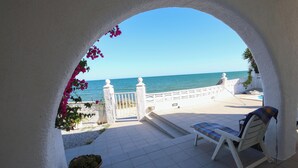 Un patio con una silla blanca, un cactus en maceta y vista al mar a través de un arco.