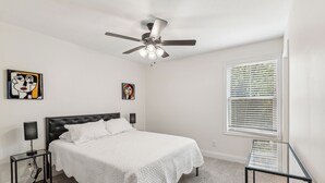 Ein Schlafzimmer mit einem Bett, einem Deckenventilator, zwei Wandlampen und einem Fenster mit Jalousien.