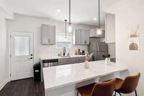 Une cuisine moderne avec des meubles blancs, un plan de travail blanc et un îlot central doté de sièges.