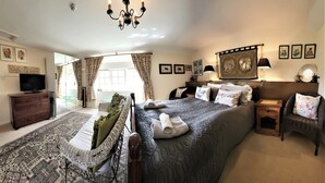 A well-lit bedroom with a large bed, a television, a wicker chair, and a patterned rug. - Escape the Ordinary - Dorset Village Vacation (Dorchester)