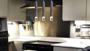A modern kitchen with stainless steel appliances, a clock on the wall, and hanging utensils. - Escape the Ordinary - Dorset Village Vacation (Dorchester)