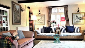 A cozy living room with a brown sofa, a wicker sofa, and a glass coffee table. There are bookshelves, a fireplace, and two framed pictures on the wall. - Escape the Ordinary - Dorset Village Vacation (Dorchester)