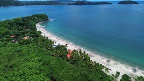 Vista aérea de una playa con abundante vegetación y aguas azul cristalino.