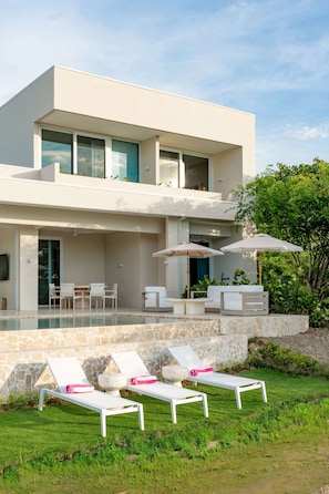 Une maison moderne à deux étages, dotée d’une piscine, d’un espace salon extérieur et d’une pelouse bien entretenue.