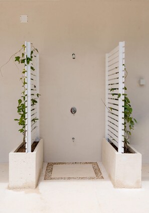 A door with two white vertical garden structures on either side, a small step leading to the door, and a simple wall-mounted light fixture above.