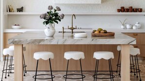 Una cocina moderna con encimera de mármol, una isla central con taburetes, una lámpara colgante y un salpicadero con detalles decorativos.