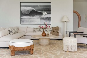 A living room with a large wave painting, a round coffee table, a white sofa, and a lamp.