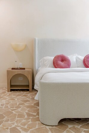 Une chambre d’hôtel bien rangée, avec un lit, une table de chevet dotée d’une lampe et une petite armoire en bois.