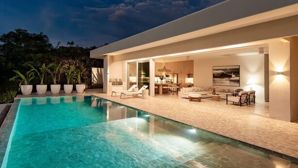 Una casa moderna con piscina, mobiliario exterior y un interior bien iluminado.