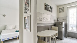 Una cocina compacta con refrigerador, una mesa de comedor con sillas y una cama con cubierta blanca.