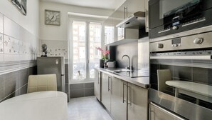 Una cocina moderna con electrodomésticos de acero inoxidable, encimera blanca y ventana con vistas a edificios.