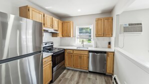 Una cocina moderna con electrodomésticos de acero inoxidable, armarios de madera y una ventana con persianas.