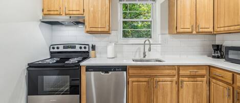 A modern kitchen with wooden cabinets, stainless steel appliances, a dishwasher, and a window with a view of greenery.