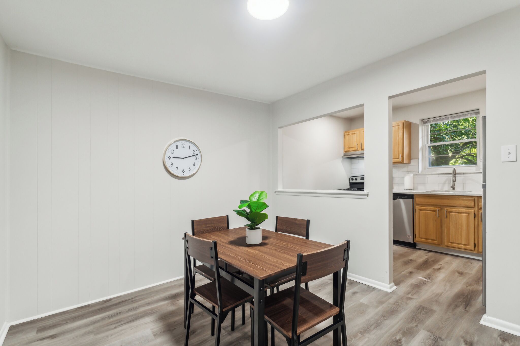 A dining area with a wooden table and chairs, a potted plant, and a wall clock.
