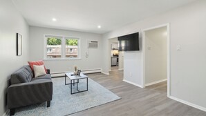 Een moderne woonkamer met een grijze bank, een bijzettafeltje en een blauw vloerkleed. Achtergrond zichtbaar van een keuken.