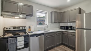 Una cocina moderna con electrodomésticos de acero inoxidable, armarios grises y un ventanal que proporciona luz natural.