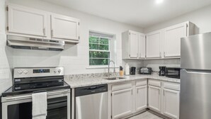 A modern kitchen with white cabinets, stainless steel appliances, a granite countertop, and a window with a view of greenery.