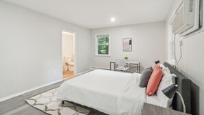 A modern bedroom with a large bed, a desk, and a window.