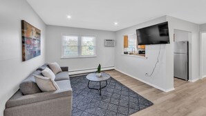 Una sala moderna con un sofá gris, una mesita redonda y un televisor grande.