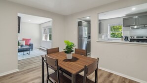 A modern kitchen with stainless steel appliances, a dining area with a wooden table and chairs, and a view of the outdoors through a window.